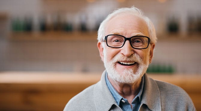 Restorative-Dentistry-Bucket Older man with glasses and white beard smiling indoors showing restorative dentistry procedures
