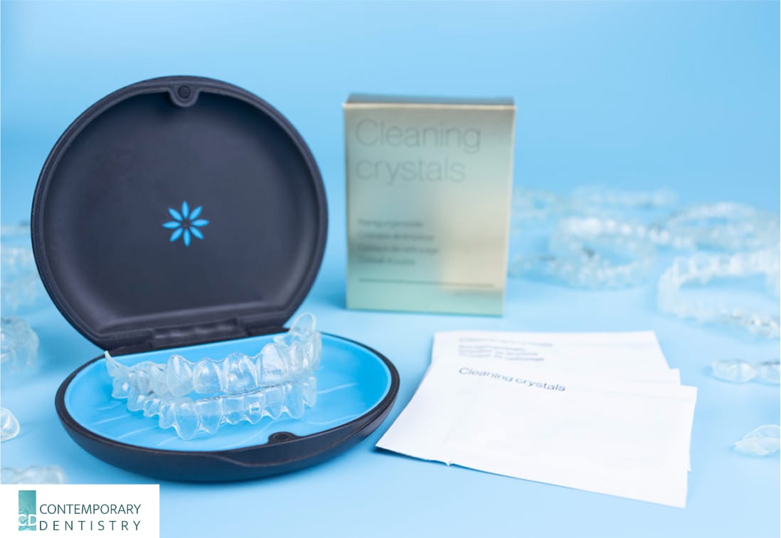 A set of clear aligners sits in a black and blue case next to cleaning crystals packets.